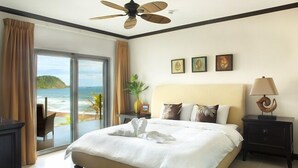 A bedroom with a bed, a ceiling fan, a nightstand, a lamp, and a view of the beach. - Manhattan hits Jaco 3br/3.5 ba Panoramic Ocean Views (Jaco)