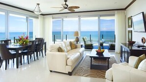 A spacious living room with a large window overlooking the ocean, a white sofa, a dining table with chairs, and a ceiling fan. - Manhattan hits Jaco 3br/3.5 ba Panoramic Ocean Views (Jaco)