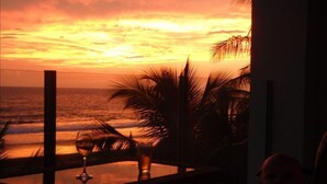 A sunset view from a balcony with a glass table, palm trees, and a chair. - Manhattan hits Jaco 3br/3.5 ba Panoramic Ocean Views (Jaco)