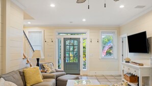 Uma sala de estar com um sofá seccional, uma mesa de centro, uma televisão e uma porta com vista para o exterior.