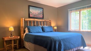 A bedroom with a wooden headboard, a large bed with blue bedding, two bedside lamps, and a window with blinds. - Beautiful view*Heated Pool*Private*Near Pic Rocks (Christmas)