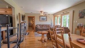 A spacious living area with a wooden dining table, chairs, and a sofa. A kitchen area with a refrigerator and cabinets is visible in the background. - Beautiful view*Heated Pool*Private*Near Pic Rocks (Christmas)