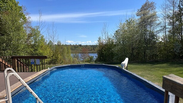 A clear blue swimming pool with a wooden deck and a view of a lake and trees. - Beautiful view*Heated Pool*Private*Near Pic Rocks (Christmas)