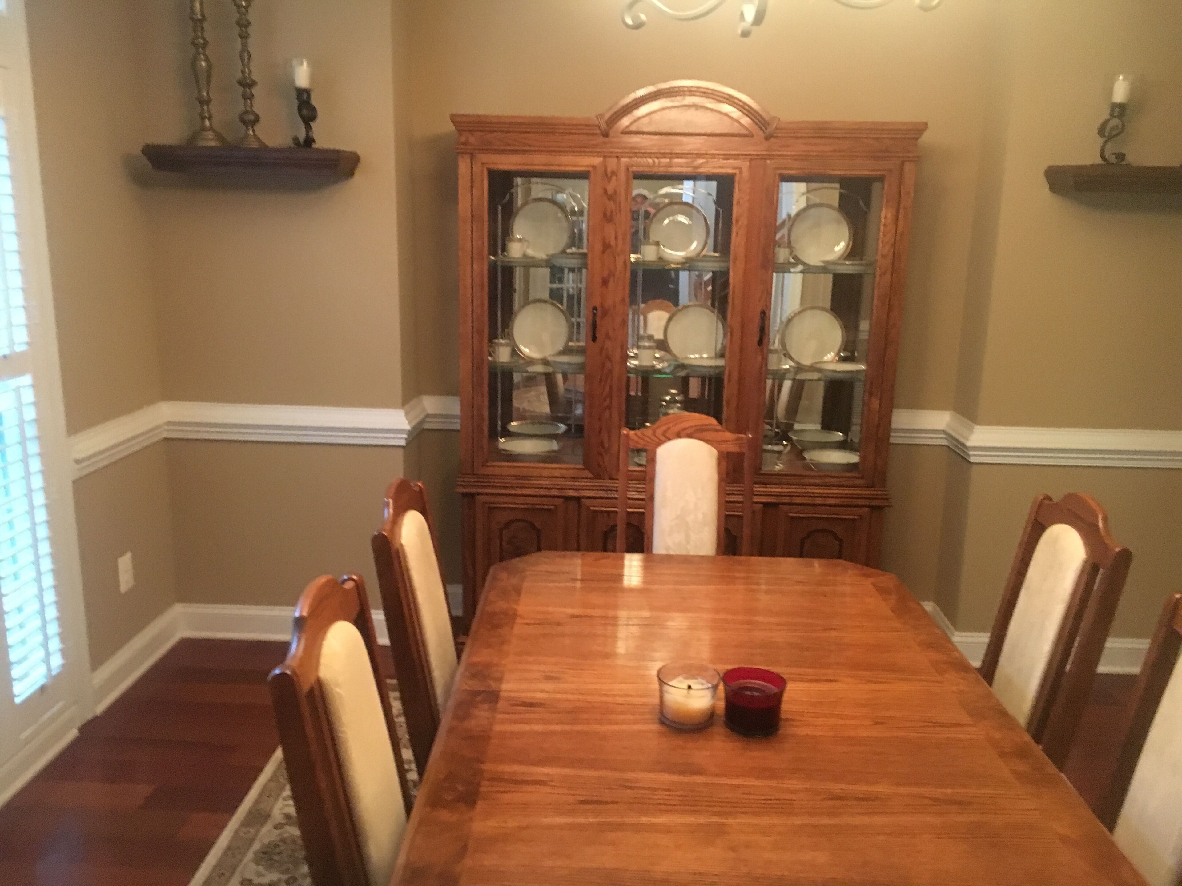 A dining room with a wooden table, chairs, a china cabinet, and two lit candles.