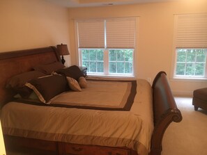 A bedroom with a large bed, two windows with blinds, a nightstand, and a lamp. - True tranquility at Lake Anna (Mineral)