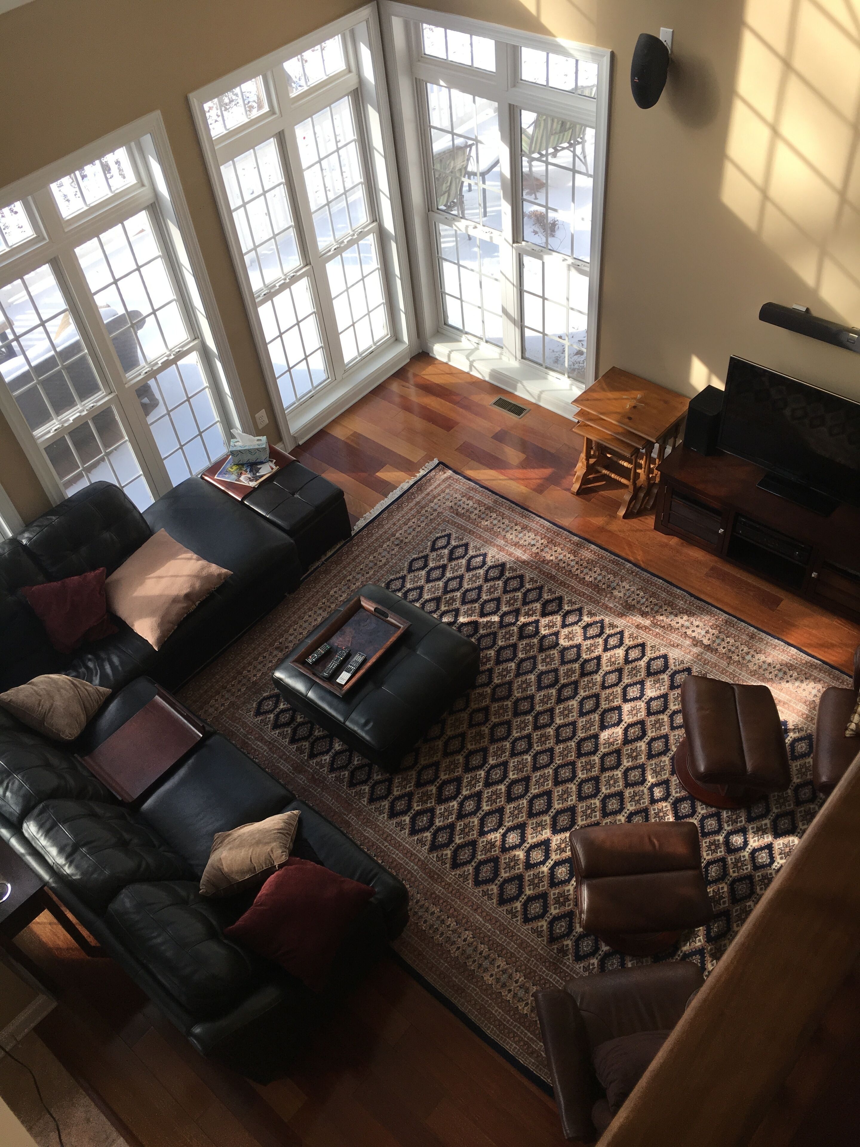 A spacious living room with a black leather sofa, a wooden coffee table, and a patterned rug. Large windows provide natural light and a view of the outdoors.
