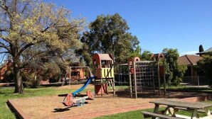 Un parc infantil amb tobogan i elements per escalar, envoltat d'herba i arbres.