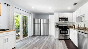 A modern kitchen with white cabinets, stainless steel appliances, and a wooden floor. - 6bdr/4bath tropical paradise with heated pool and lanai, 1 mile from the beach (Naples)