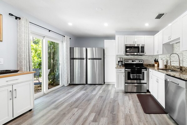 A modern kitchen with white cabinets, stainless steel appliances, and a wooden floor.