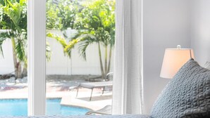 A bedroom with a view of a swimming pool, a lamp, and a textured pillow. - 6bdr/4bath tropical paradise with heated pool and lanai, 1 mile from the beach (Naples)