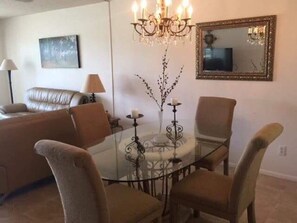 Ein Essbereich mit einem Glastisch, vier Stühlen, einer Kronleuchter, einem Spiegel und einem Sofa.