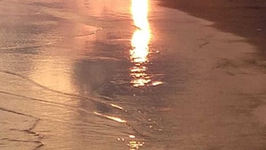 A beach scene with people walking and standing, and a sunset in the background.