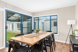 A dining area with a wooden table and chairs, large windows, and a view of a building outside.