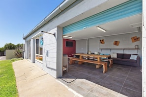 A covered patio with a wooden table and benches, a red wall, and a grey tiled floor.