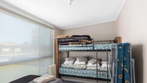 Een stapelbed met uitzicht op een gebouw, een klein tafeltje met een handdoek en een raam met zonwering.