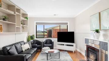 A modern living room with a fireplace, a flat-screen TV, and a large window.