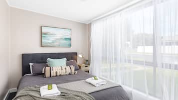 A bedroom with a bed, a bedside table, a lamp, and a window with sheer curtains.