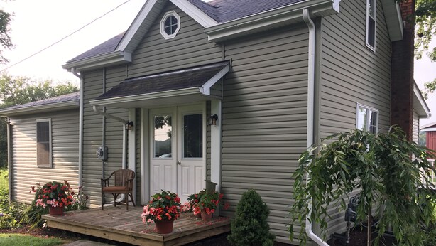A two-story house with a front porch, a small garden, and a wooden deck. - Little house on the farm (Middlefield)