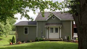 A two-story house with a front porch, a small front yard, and a tree in the foreground. - Little house on the farm (Middlefield)