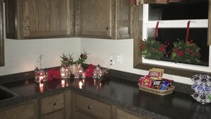 A kitchen with wooden cabinets, a window with a curtain, and holiday decorations. - Little house on the farm (Middlefield)