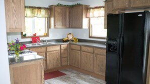 A kitchen with wooden cabinets, a black refrigerator, a sink, and a red rug. - Little house on the farm (Middlefield)