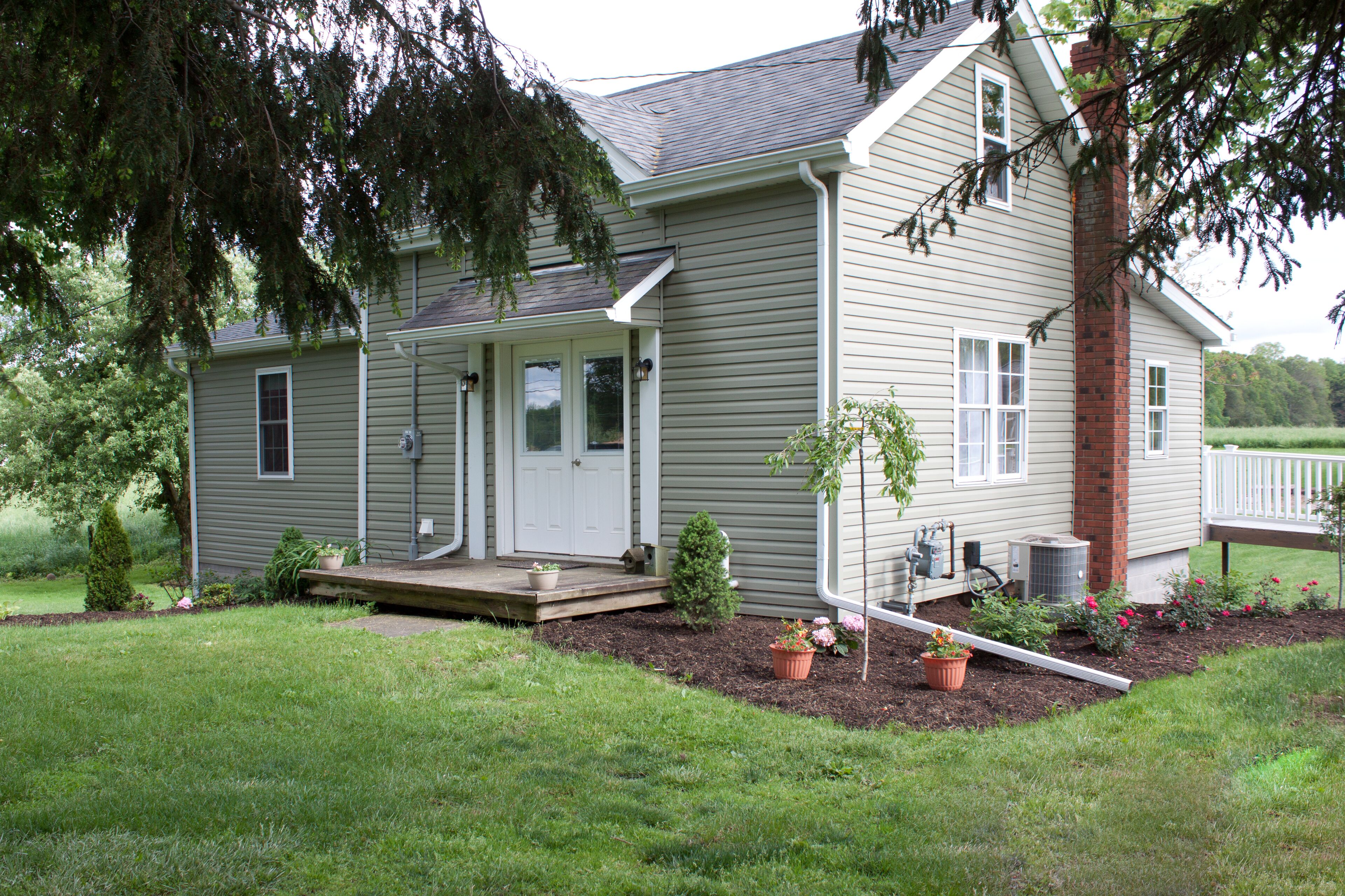 A two-story house with a front porch, a brick chimney, and a small garden with potted plants.