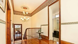 A wooden-floored hallway with a staircase, a chandelier, and a decorative wall panel. - Hindmarsh House on College | Steps to Glenelg Beach, Cafes & Jetty Road (Glenelg)