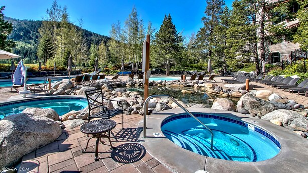 Un área de piscina con varios jacuzzis, sillas de descanso y vistas a un paisaje montañoso.