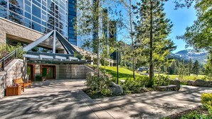 Un edificio moderno con fachada de vidrio, asientos exteriores y un área ajardinada con árboles y rocas.