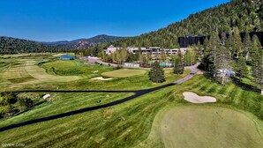 Un campo de golf con un club de campo, un estanque y una ladera boscosa.