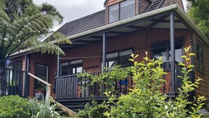 Een tweelaags huis met een houten gevel, een overdekte veranda en een omheinde tuin met verschillende planten.