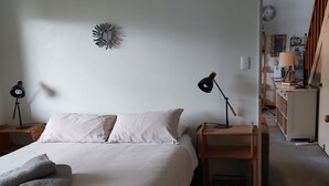 Een netjes opgemaakt bed met kussens en een opgevouwen handdoek, een bedlampje, een wanddecoratie en een deur naar een andere kamer.