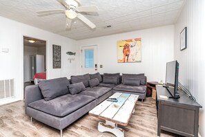A modern living room with a sectional sofa, a coffee table, a television, and a ceiling fan. - Ruff Life - Classic Island Cottage - 4 BR and Easy Beach Access. Dog Friendly! (Surf City)