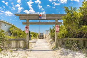 A wooden boardwalk leading to a beach entrance with no parking signs on either side.