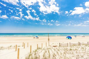 A beach with a wooden fence, a sandy area, and a clear blue sky.