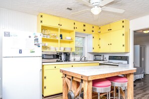 A kitchen with yellow cabinets, a white refrigerator, a wooden table with two stools, and various kitchen appliances. - Ruff Life - Classic Island Cottage - 4 BR and Easy Beach Access. Dog Friendly! (Surf City)