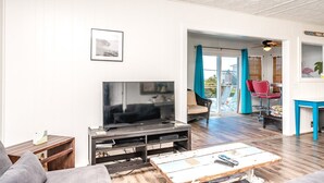 En stue med fjernsyn, sofa og spiseplads med stole.