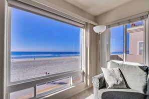 A room with a large window overlooking a beach, a sofa with cushions, and a floor lamp.