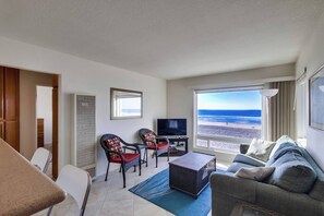 Quarto de hotel com vista para a praia, uma televisão, um sofá e duas poltronas.