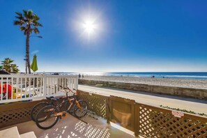 Uma varanda com uma bicicleta, vista para a praia e céu limpo.