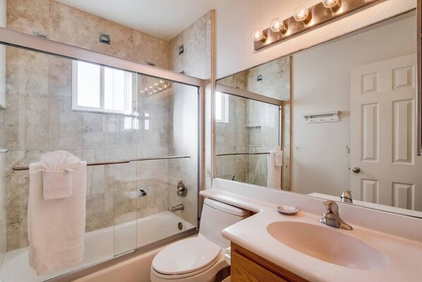 A modern bathroom with a glass-enclosed shower, a white toilet, a vanity with a sink, and a large mirror.