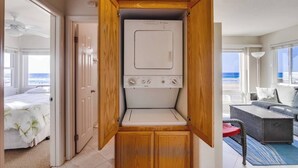A laundry room with a front-loading washer and dryer, wooden cabinets, and a view of the ocean.