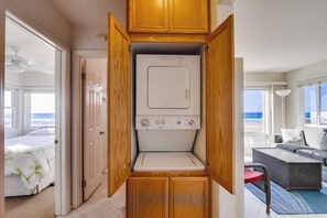A laundry room with a front-loading washer and dryer, wooden cabinets, and a view of the ocean.
