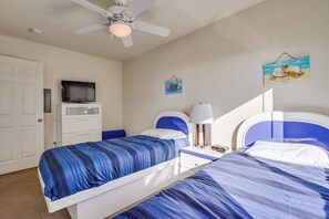 A bedroom with two beds, a television, a ceiling fan, and a wall-mounted picture.