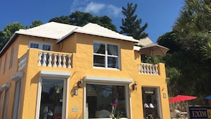 Een tweelaags gebouw met een gele gevel, een balkon op de bovenverdieping en een etalage met borden die een juwelenwinkel en een woondecoratiewinkel aangeven.
