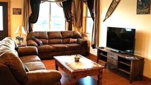 A living room with a brown leather sofa, a wooden coffee table, a flat-screen TV, and curtains.