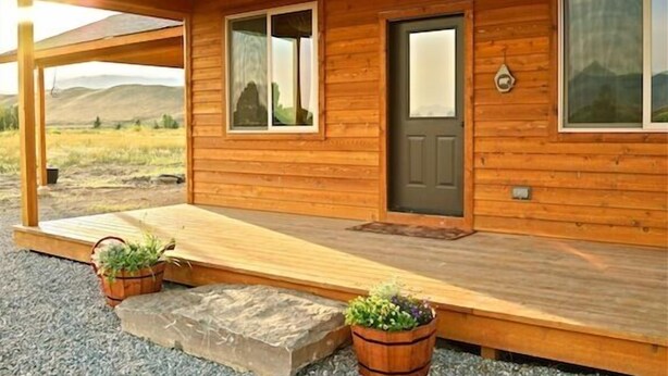 A wooden cabin with a porch, large windows, and a door.