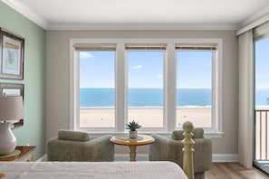 A room with a bed, two armchairs, a small table, and a view of the beach through large windows. - 🏖️  Oceanfront Boardwalk unit w/ Pool Just Renovated steps to Downtown Events 🏖️ (Ocean City)