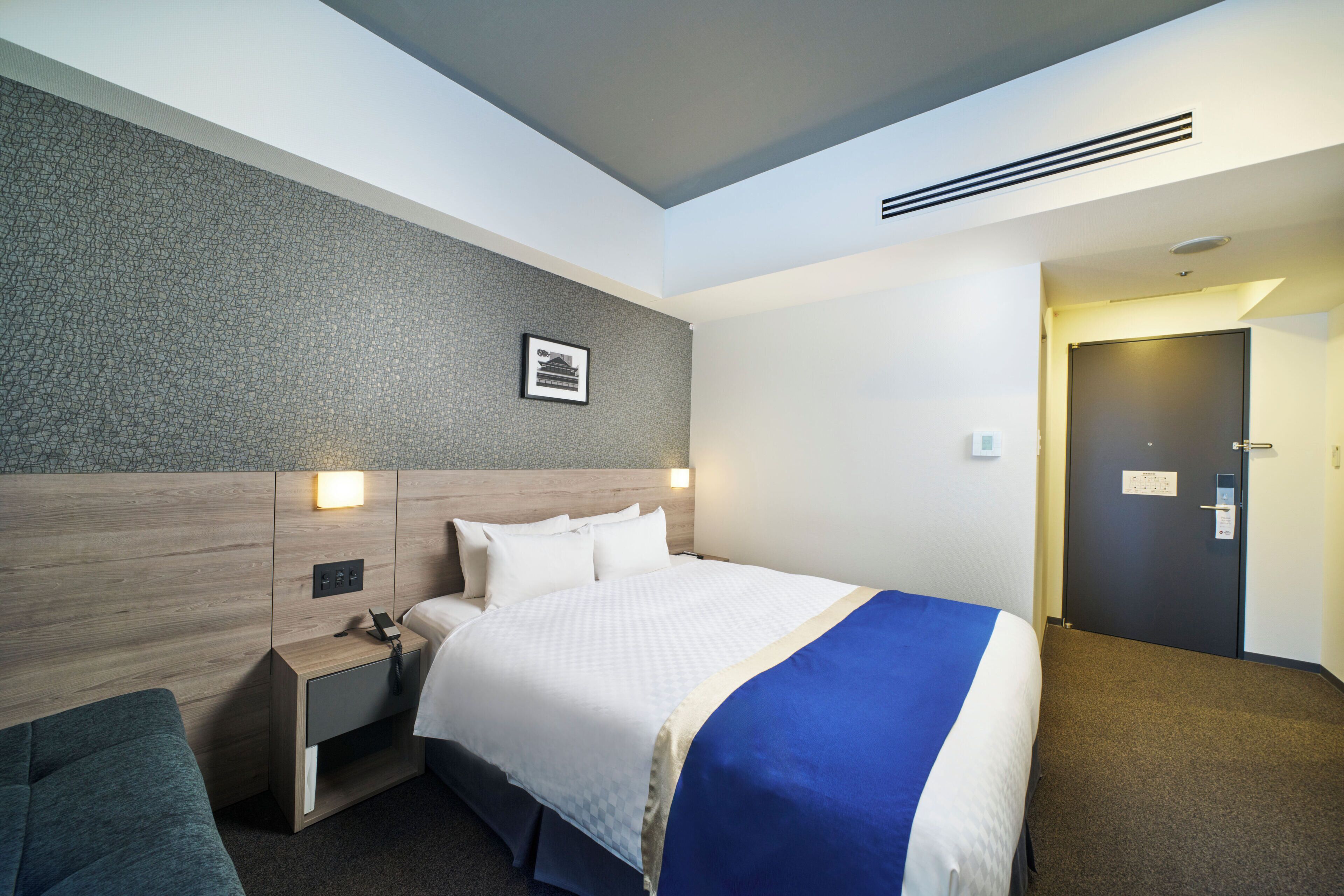 Una habitación de hotel con una cama grande, un cabecero de madera, una mesita de noche, un escritorio, una silla y una puerta.