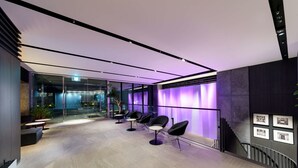 Un espace d’attente moderne avec un mur en verre, des chaises noires et un mur éclairé de couleur violette.